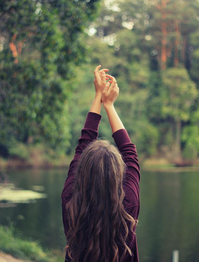 Woman with arms over head near lake | Woman smiling and holding camera | Therapy for Codependency